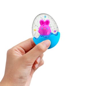 SQTEND25_Image3 A hand is holding a small, clear, egg-shaped snow globe like squishy toy with a blue base. Inside the globe is a pink bunny with a smiling face and colorful stars floating around it. The background is plain white.